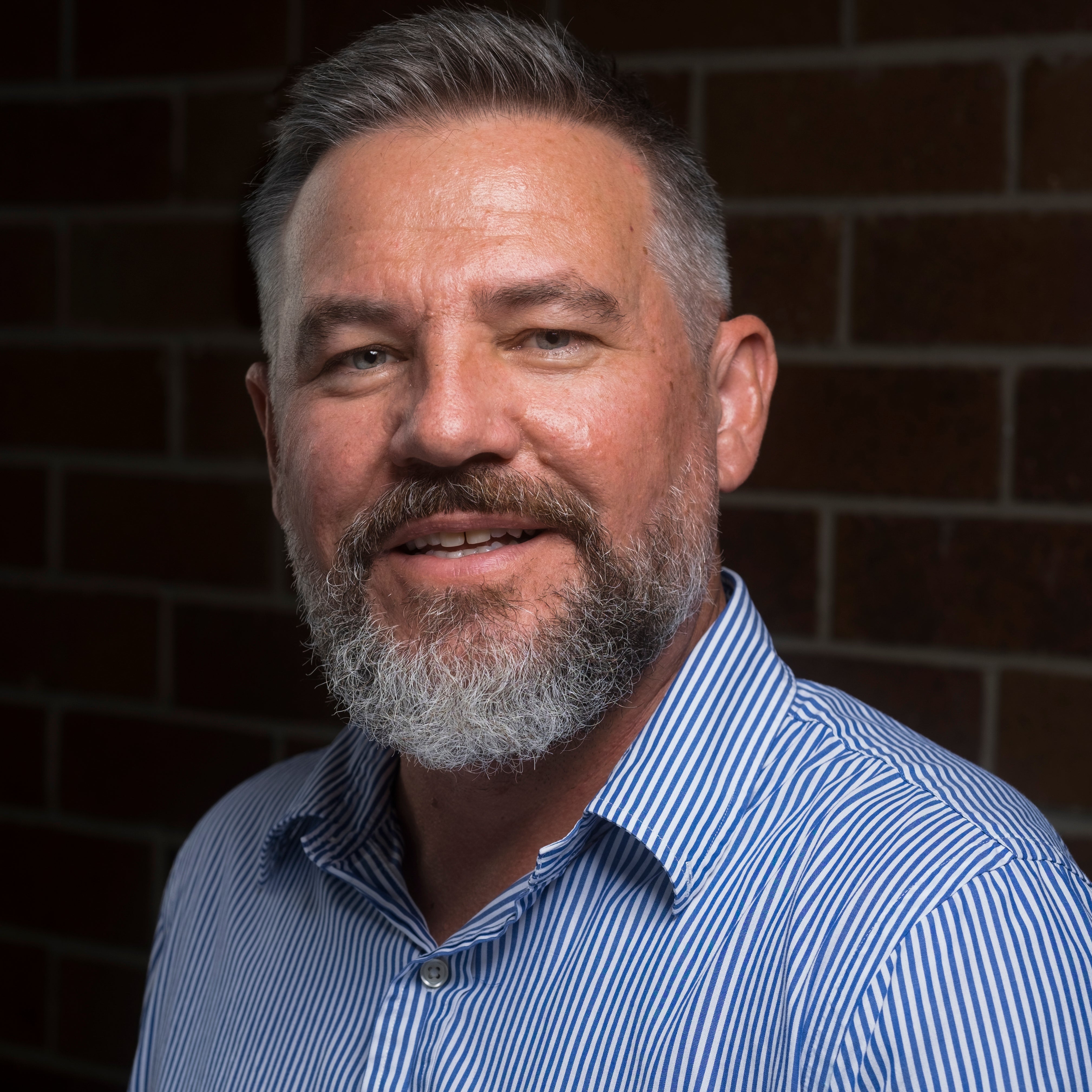 Mathew Dow wearing a blue striped shirt against a brick wall